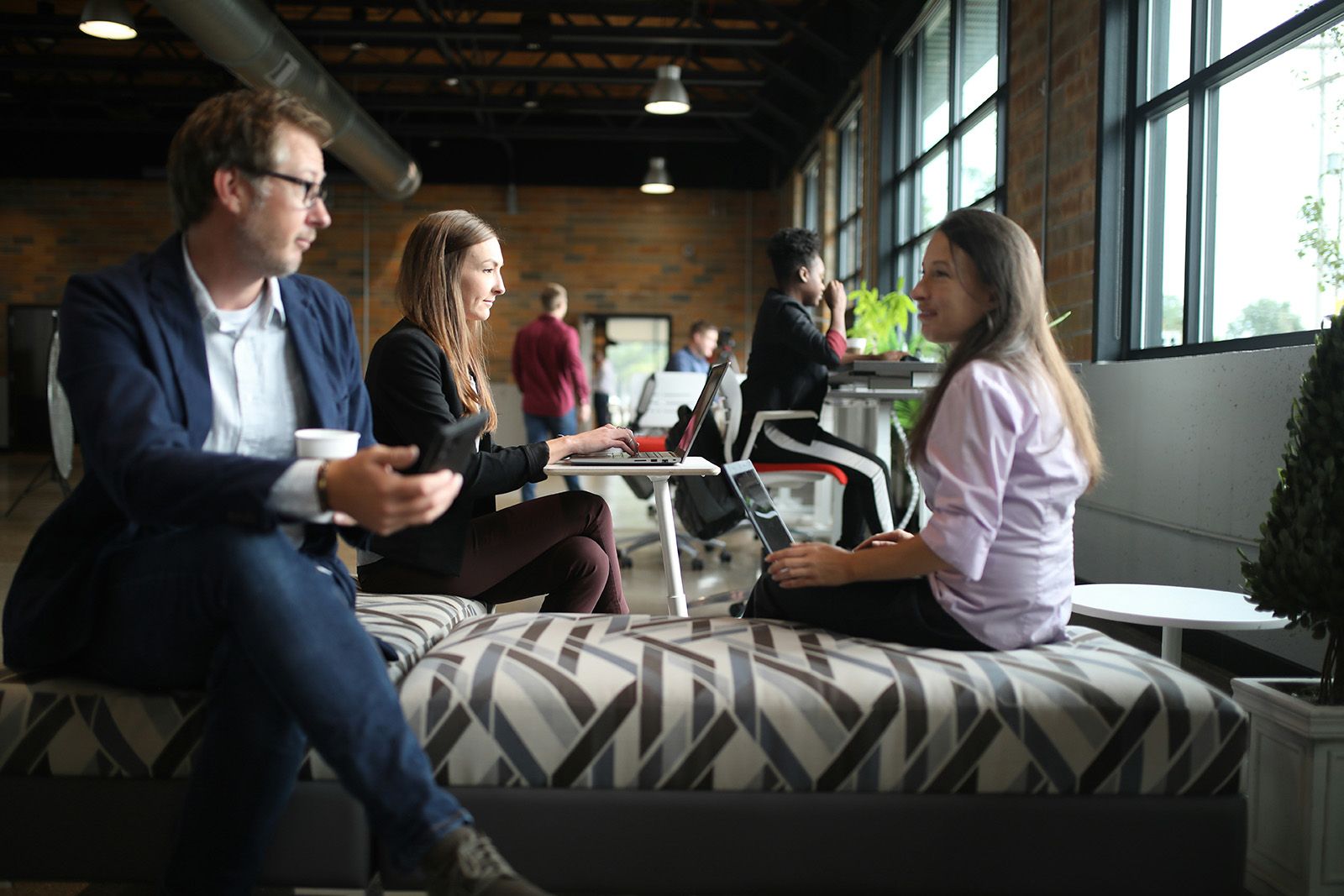 Coworkers talking and working on laptops in an open brick-walled office